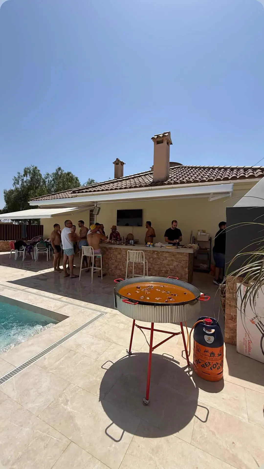 Paella en marcha junto a la piscina mientras los invitados charlan